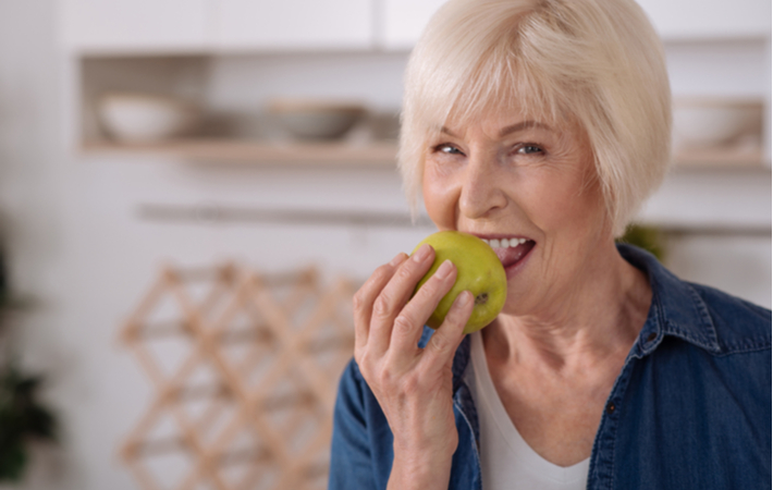 older woman smiling and eating a green apple